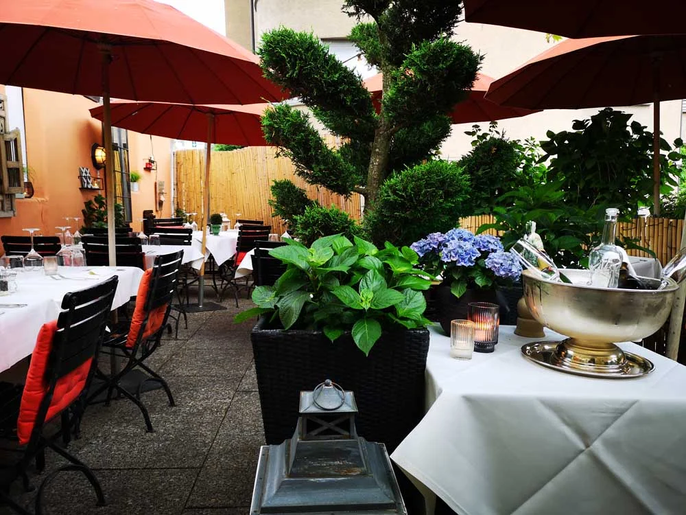 Die begrünte Gartenterrasse mit gedeckten Tischen und roten Sonnenschirmen